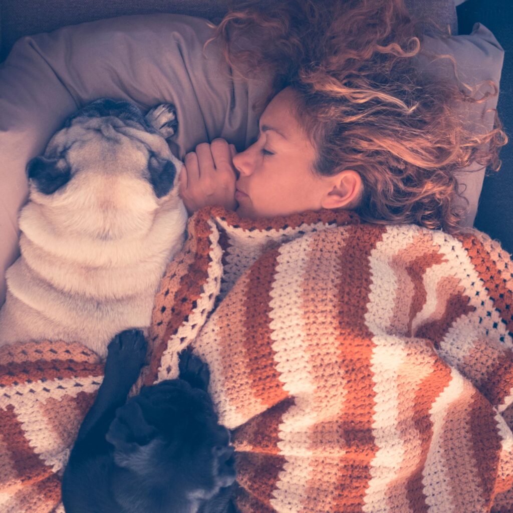 Woman under a blanket snuggling up with her two dogs, they are all asleep